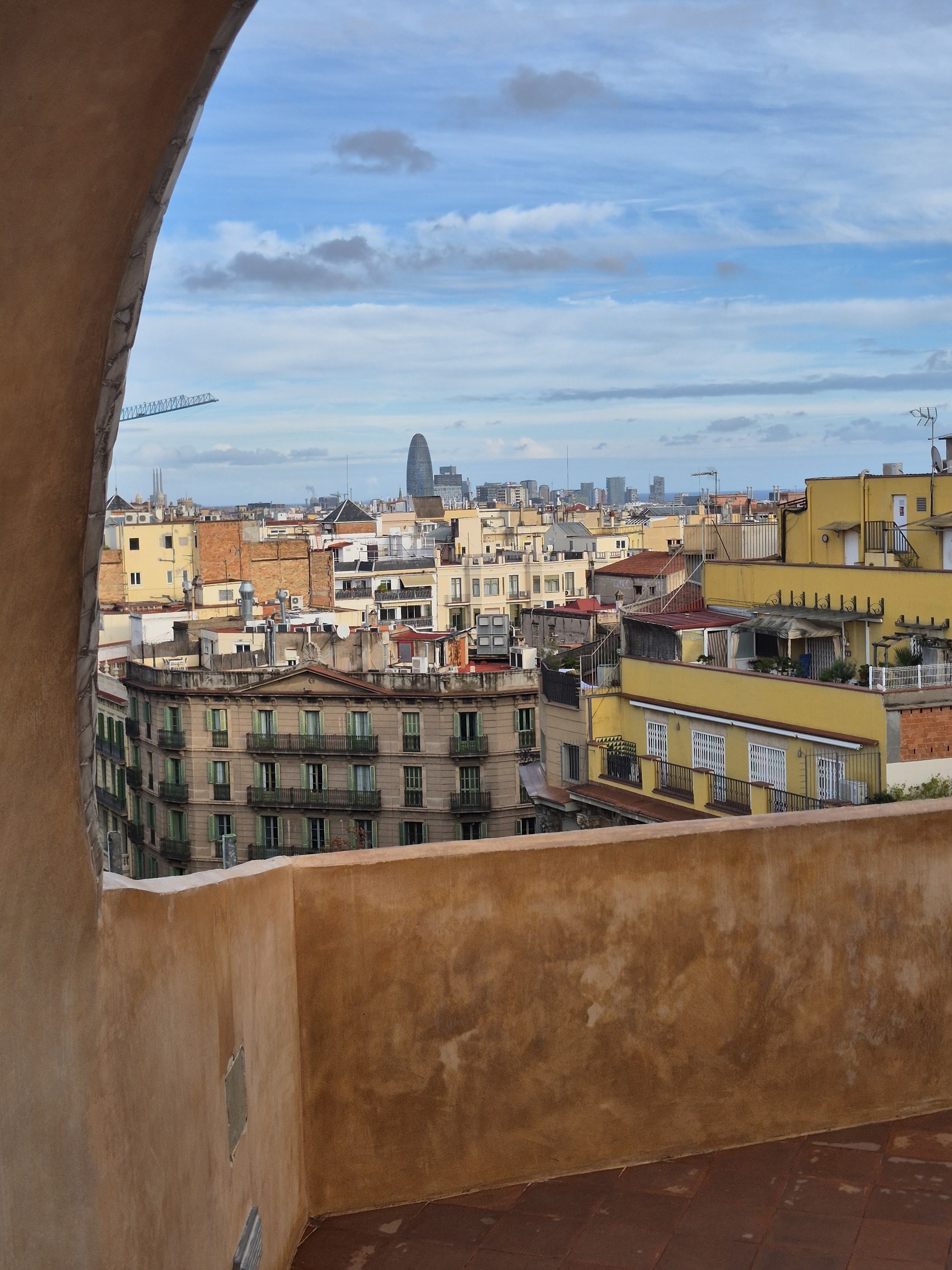 The undulating rooftop of Casa Milà, Gaudí's stone chimneys framing a view over the terracotta rooftops of the Eixample toward the Sagrada Família