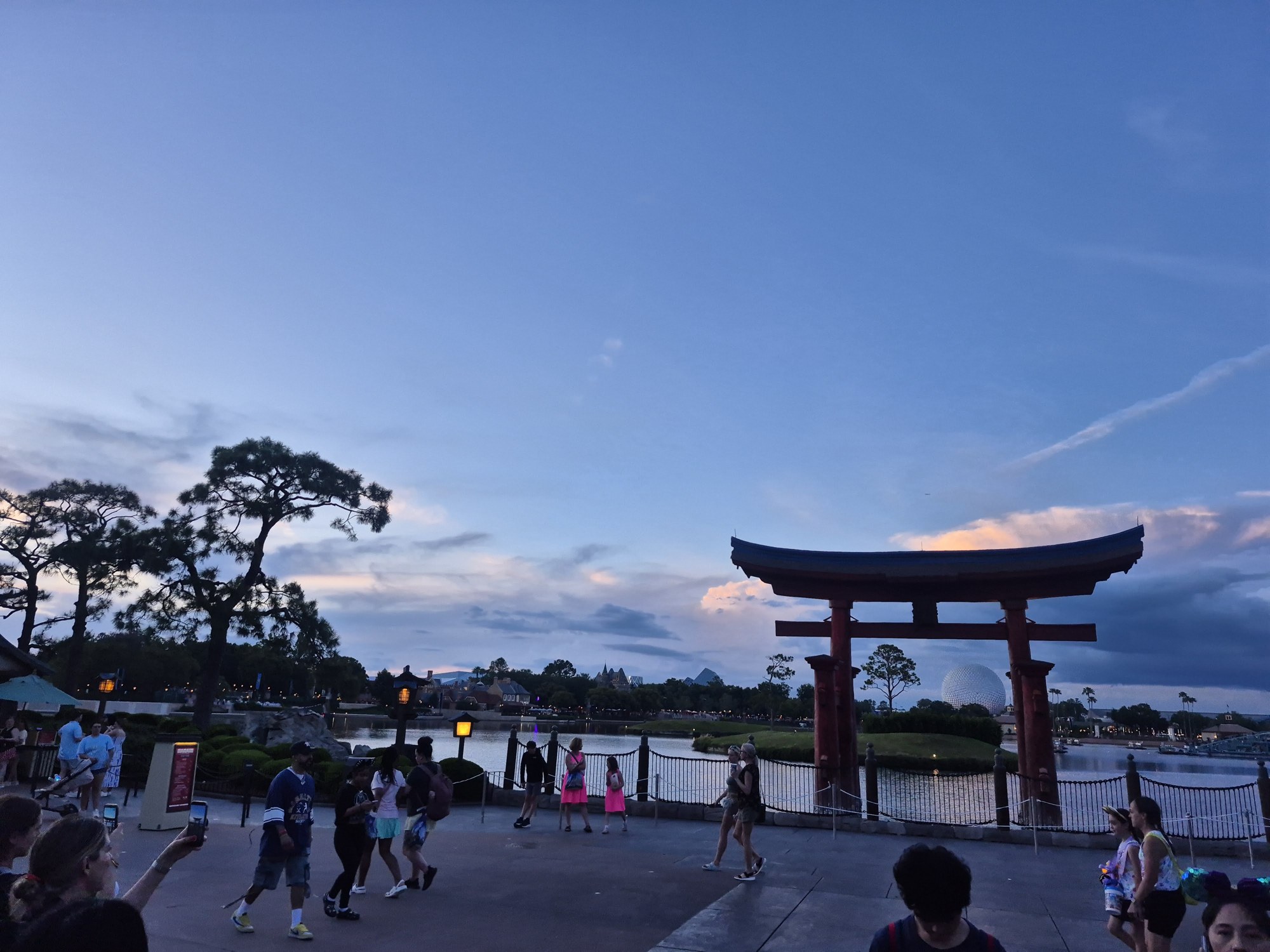 The Japan pavilion's red torii gate at the edge of the World Showcase lagoon at EPCOT, at dusk, with people along the waterfront