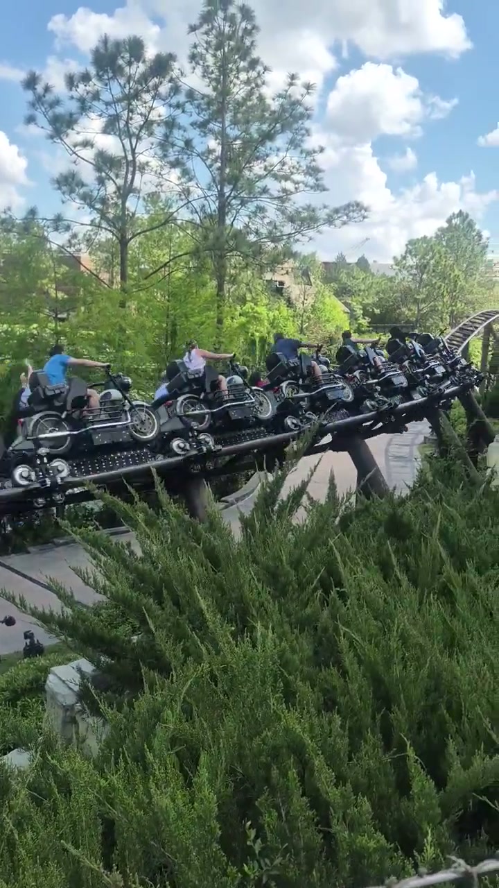 A coaster train on Hagrid's Magical Creatures Motorbike Adventure threading past the ruined castle arches at Islands of Adventure, under a blue sky with big clouds